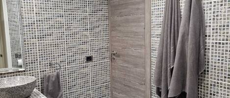 Un baño con pared de mosaicos, puerta de madera, lavabo, toallero y un inodoro.