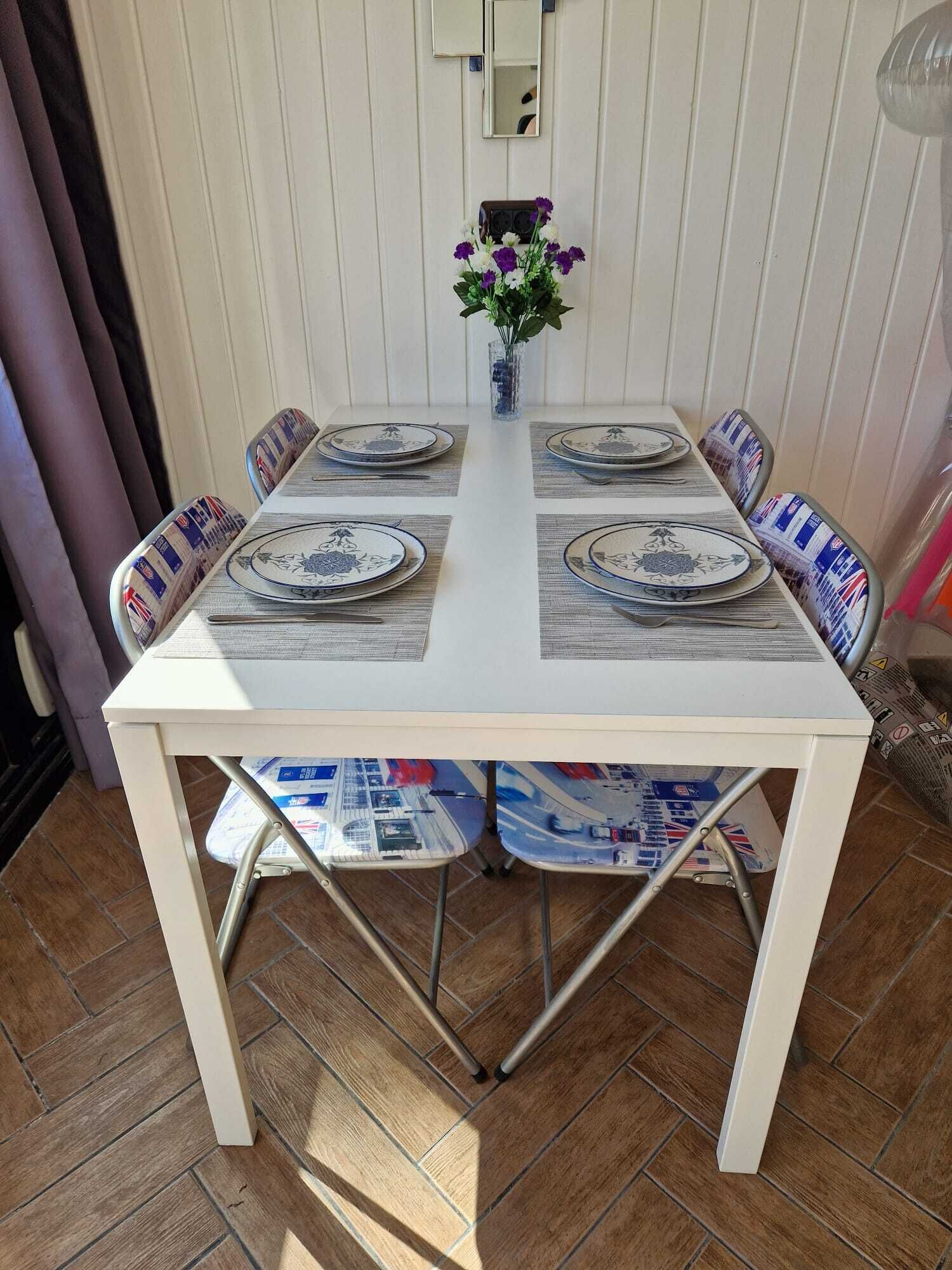 A dining table with four chairs, each with a patterned cushion. A vase with purple flowers is placed on the table.