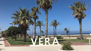 Un chemin pavé bordé de palmiers et un grand panneau blanc sur lequel on peut lire le mot « VERA ».