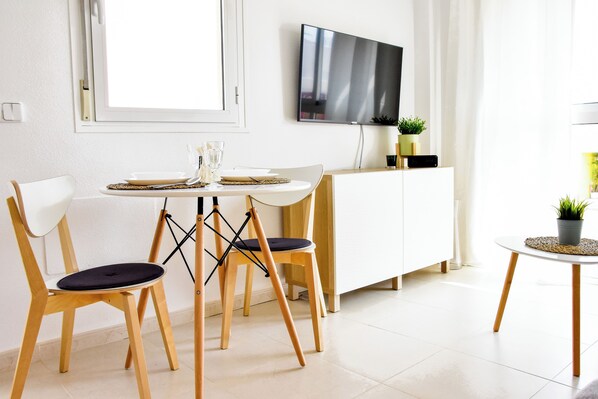 A modern dining area with a white table, two wooden chairs, a TV mounted on the wall, and a small potted plant on the sideboard. - Manzanilla Penthouse, Private Jacuzzi & 5min Beach (Vera)