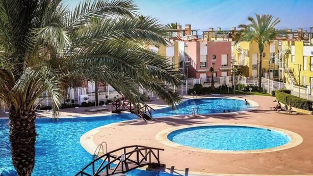Un complexe hôtelier doté de plusieurs piscines, de palmiers et d’un pont reliant les différentes piscines.