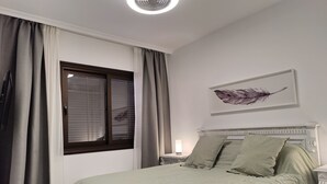 Ett sovrum med en säng, ett fönster med gardiner, ett nattduksbord med en lampa och ett konstverk som hänger på väggen.