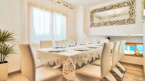 Un coin repas avec une table dressée pour six personnes, des chaises blanches et un grand miroir décoratif au-dessus de la table.