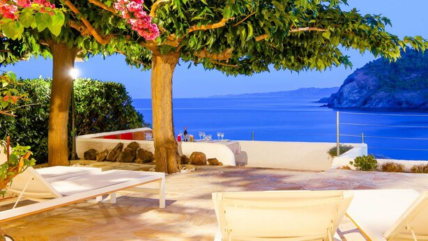 Une terrasse avec des fauteuils de jardin blancs, une table et une vue sur la mer.