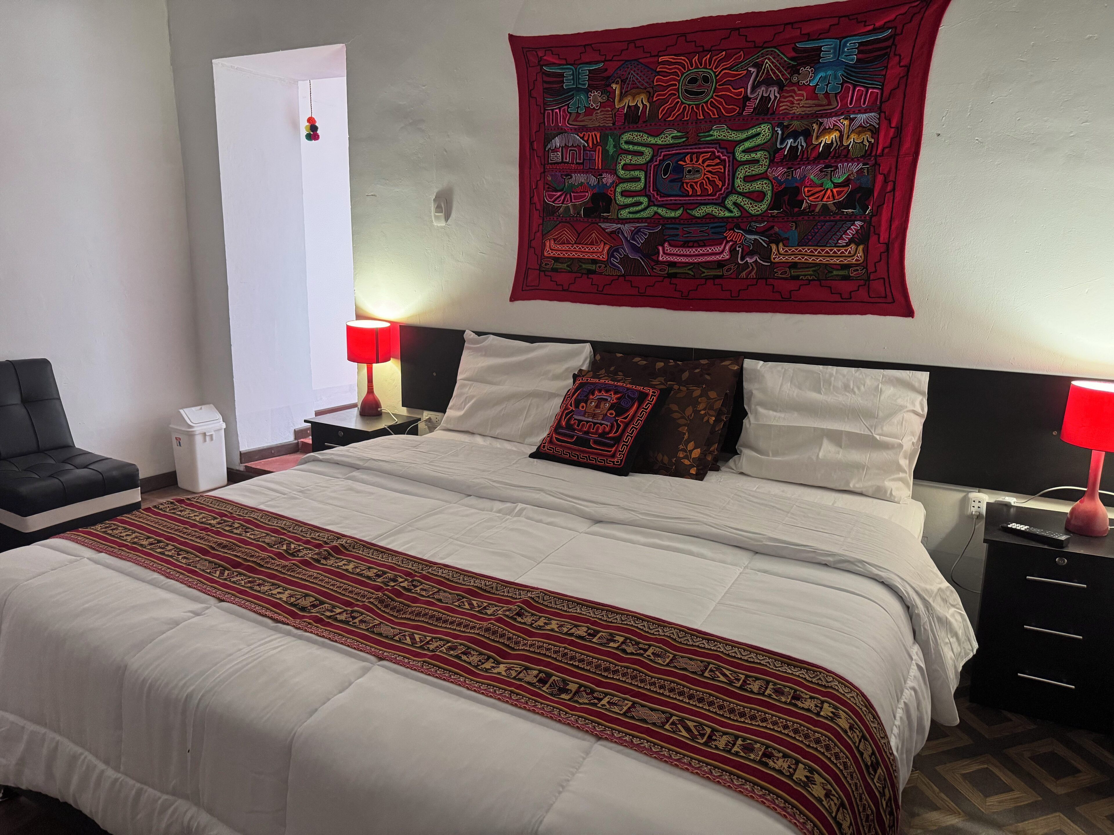 A hotel room with a large bed, two bedside tables, a chair, and a tapestry on the wall.