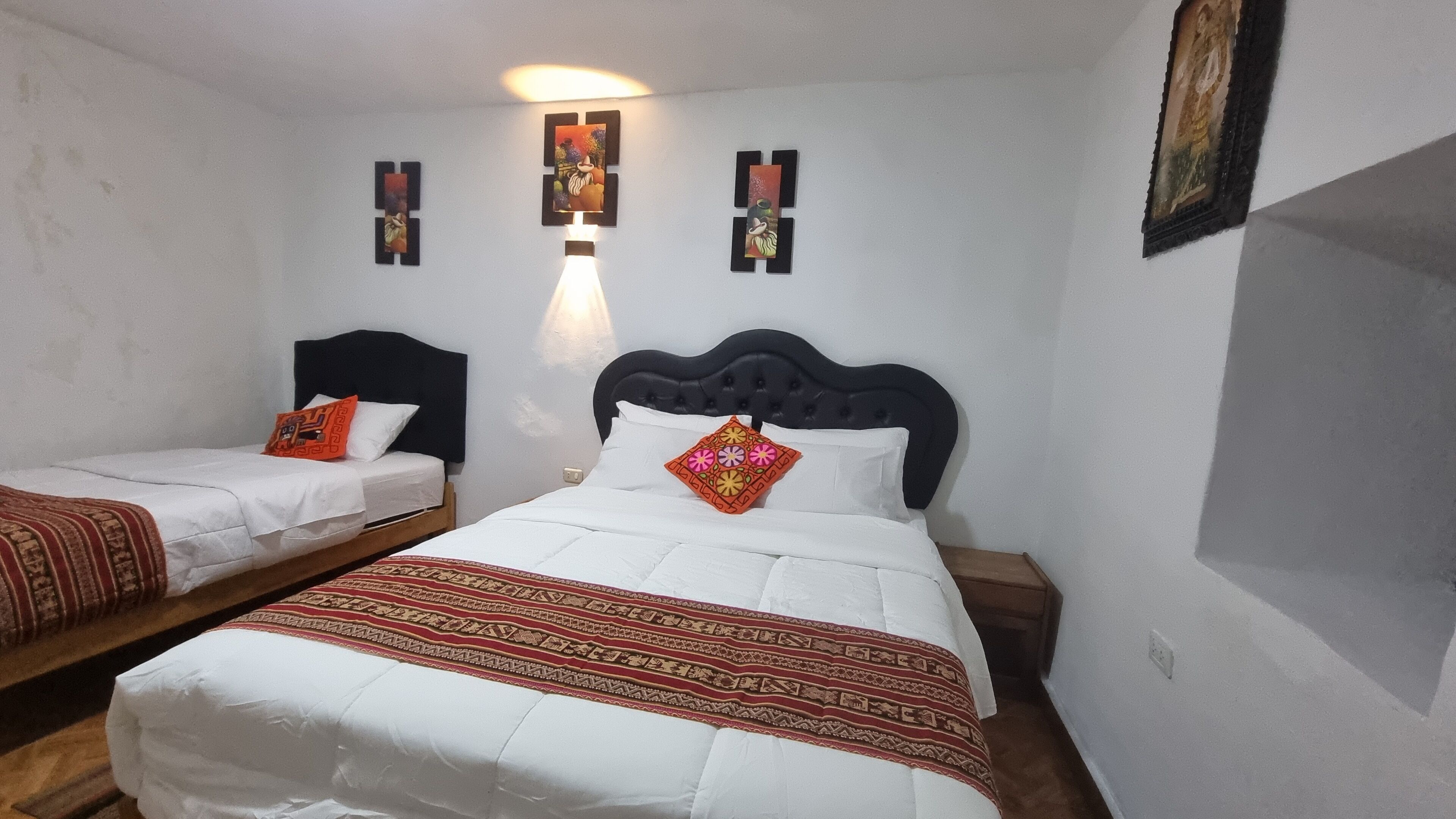 Quarto pequeno e limpo com duas camas, cada uma com cabeceira e almofadas. Há obras de arte nas paredes acima das camas.