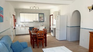 A modern kitchen with white cabinets, a dining area with wooden chairs, a washing machine, and a white refrigerator. - Beachfront House,sea Views Near Historic Cartagena (Cartagena)
