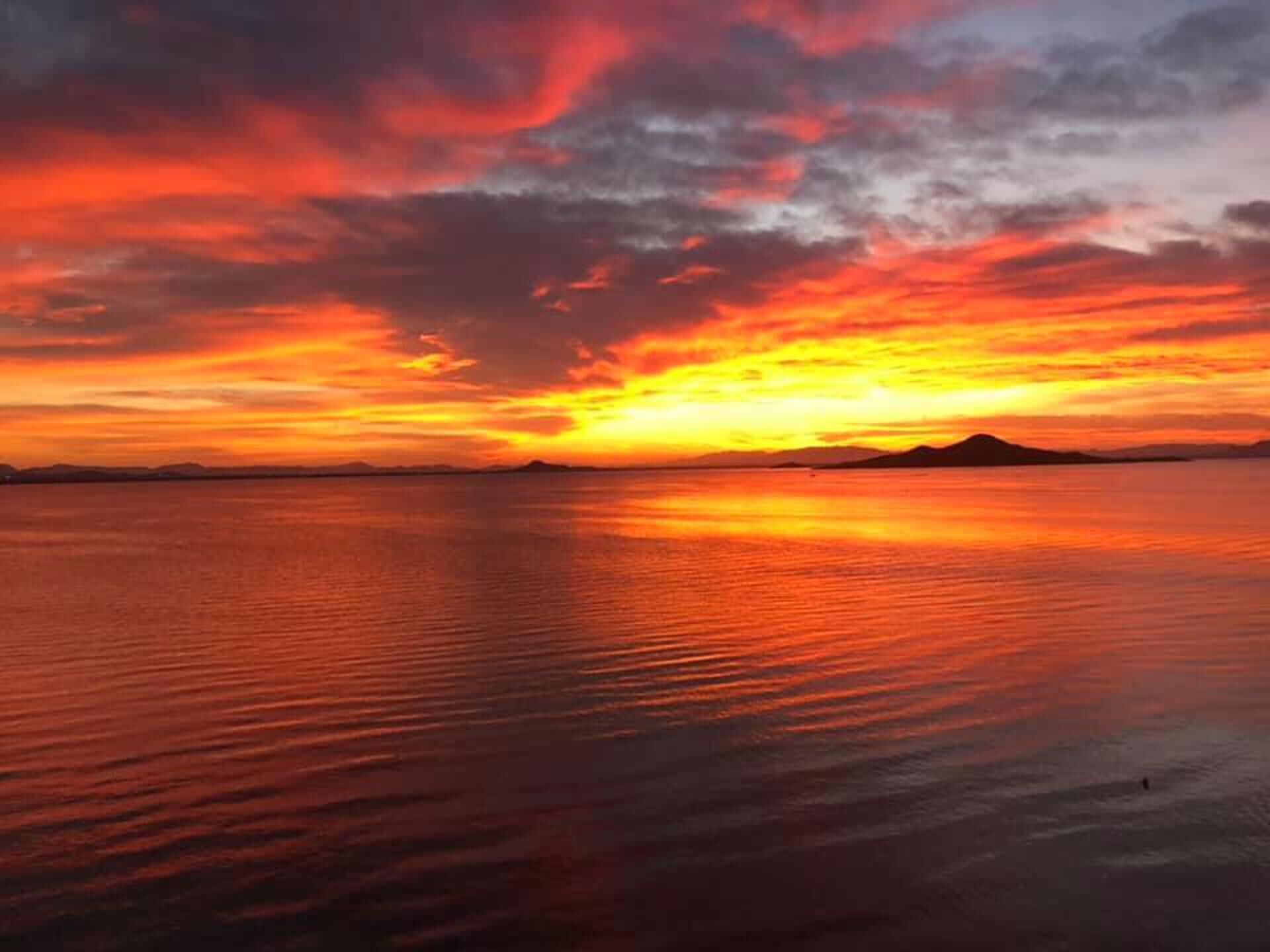 Um pôr do sol sobre águas calmas, com uma cadeia de montanhas ao longe.
