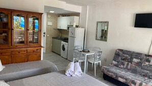 Un ambiente compatto con angolo cottura, zona pranzo e divano con decorazioni a tema viaggio.
