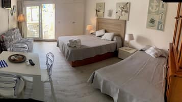Ein Hotelzimmer mit zwei Betten, einem Esstisch mit Stühlen und einem kleinen Tisch mit Korb und Fernbedienungen.