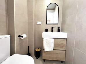 Un baño moderno con inodoro, lavabo, espejo y toallero.