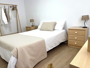 Un dormitorio ordenado con cama, mesitas de noche, lámpara y un perchero.