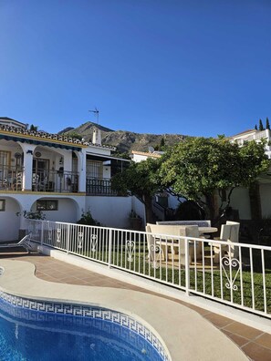 A pool area with a white fence, a dining table with chairs, and a building with a balcony in the background. - Captivating Private House in Benalmadena (Benalmádena)