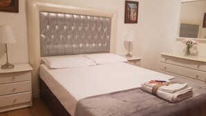Een keurig opgemaakt bed met een gestuufd hoofdbord, een nachtkastje met een lamp, een kaptafel en een spiegel aan de muur.