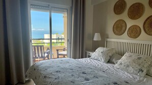 Une chambre avec un grand lit, un balcon avec des chaises et une vue sur la mer.