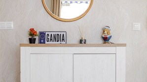 Un armadio bianco con uno specchio sopra, un cartello con la scritta "GANDIA", una piccola pianta e una statuina sulla sommità.