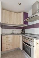 Cocina compacta con armarios de madera, pileta de acero inoxidable, cafetera y horno.