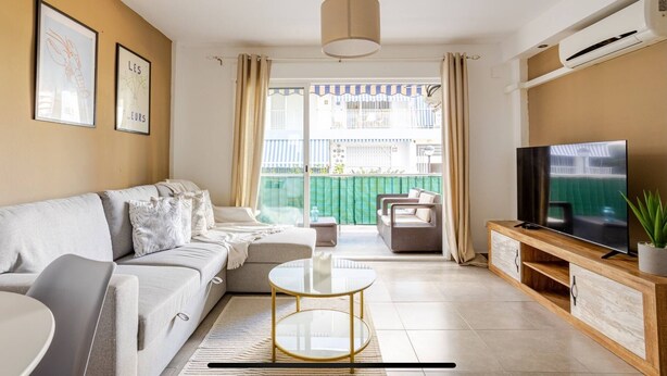 Un soggiorno con divano, tavolino, televisore e un balcone con vista.