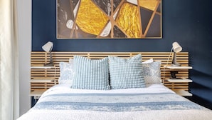 Un letto rifatto con cura, coperto da una tenda a righe blu e bianche, due abat-jour e un quadro astratto appeso alla parete, con sfumature oro e nero.