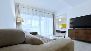 A modern living room with a sofa, a glass coffee table, and a television on a wooden cabinet. - Superior Apartment Sleeps 2 With Pool (La Oliva)
