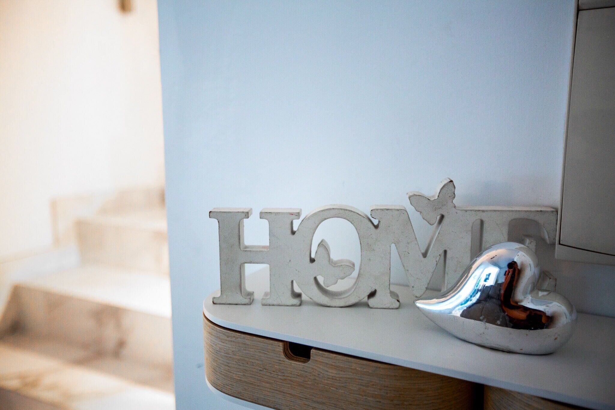 Una señal decorativa con la palabra 'HOME' y un objeto con forma de corazón sobre una superficie blanca.
