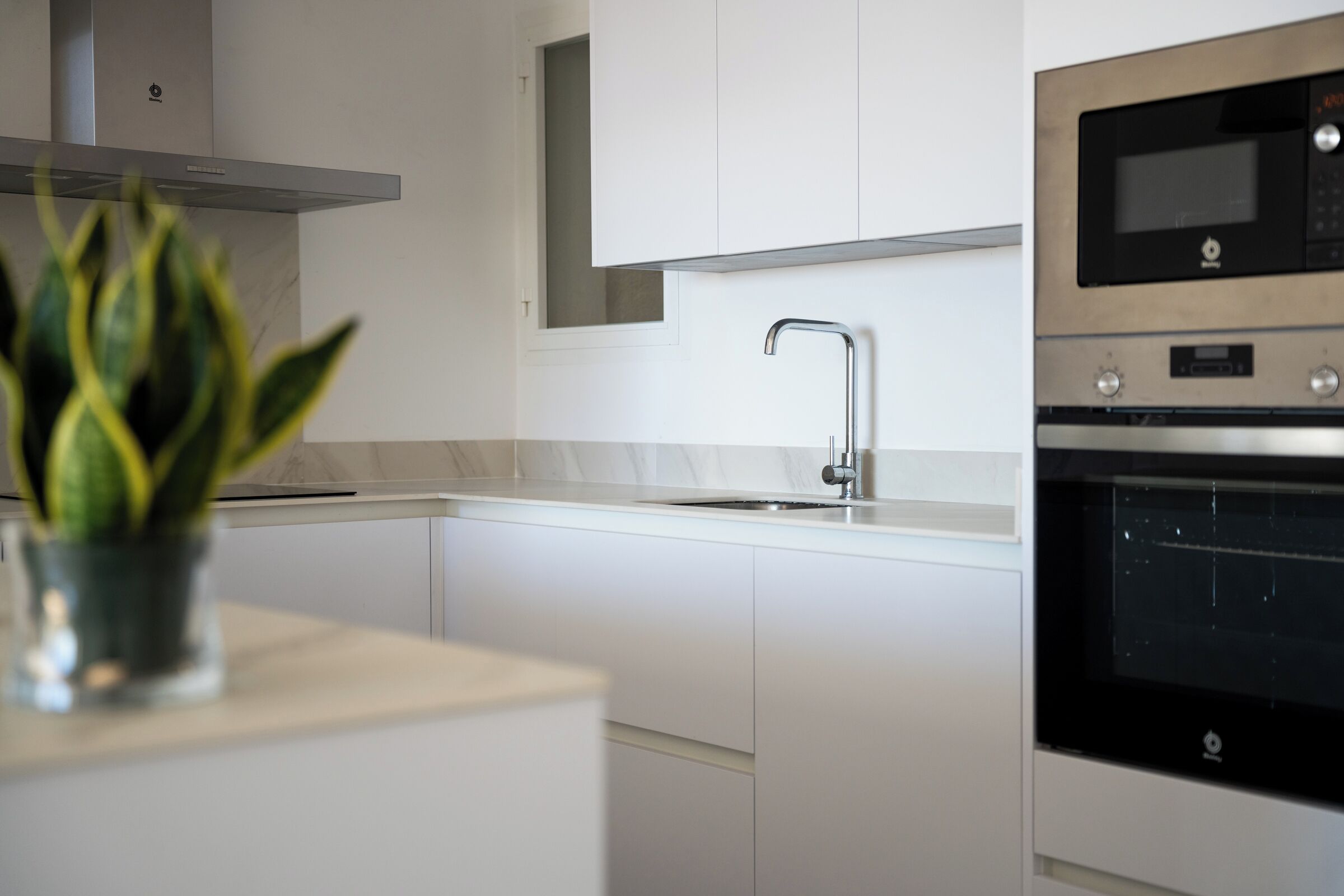 Una cocina moderna con armarios blancos, un lavamanos de acero inoxidable y un horno empotrado.