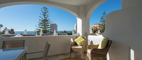 A balcony with wicker chairs, a table, and a woven rug.