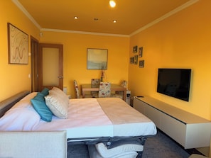 A hotel room with a bed, a desk, a chair, a TV, and a door.