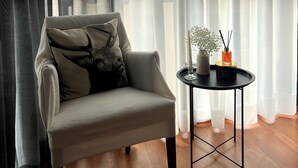Ein moderner Sessel mit Zierkissen, ein kleiner runder Tisch mit Kerze und eine Vase mit Blumen.
