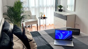 Ein modernes Wohnzimmer mit einem Laptop auf einem Schachbrettteppich, einer Couch mit gemusterten Kissen, einer Topfpflanze, einem kleinen runden Tisch mit einer Vase und einer Kommode mit Schubladen.