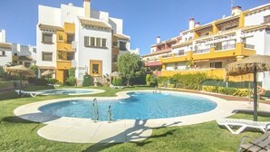 Ein Poolbereich mit Liegestühlen, einem runden Pool und mehrstöckigen Gebäuden mit Balkonen.