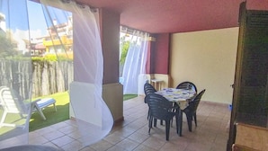 Eine Terrasse mit Tisch und Stühlen, einem weißen Vorhang und Blick auf einen Garten und Gebäude.