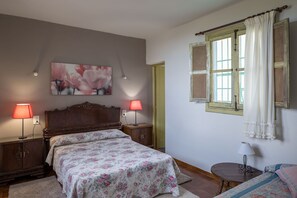 A bedroom with a wooden bed, two bedside lamps, a floral bedspread, a painting on the wall, and a window with curtains. - House Sleeps 8 - Natural Pool, Pet Friendly, Views (Nules)