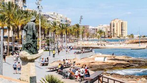 A coastal promenade with a statue, palm trees, and a beach in the background. - Amplio Apartamento Turistico en Torrevieja (Torrevieja)
