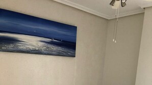A bedroom with a bed, pillows, a painting of a beach scene, and two rolled towels on the bed. - Amplio Apartamento Turistico en Torrevieja (Torrevieja)