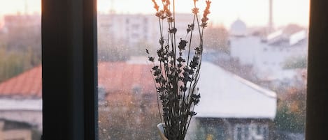 A window with a white cup and saucer, a white vase with dried flowers, and a book on a windowsill.
