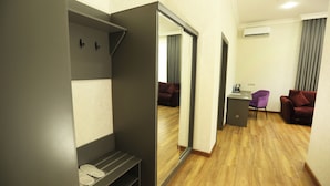 A modern hotel room with a wooden floor, a desk with a chair, a purple chair, and a red sofa. - Parklane Hotel (Tashkent)
