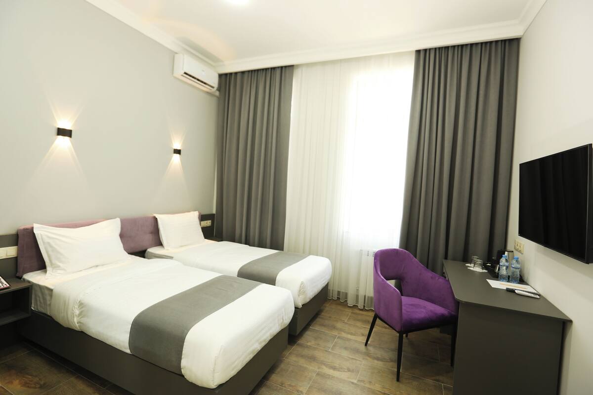 A hotel room with two beds, a desk, a chair, and a TV.