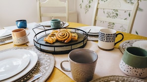A dining table set with plates, cups, and a tray of pastries. - The Leam Terrace Escape 3 Bed Townhouse (Royal Leamington Spa)