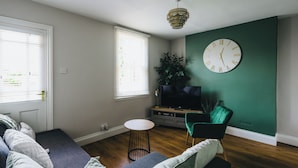 A living room with a sofa, a TV, a green wall, and a clock. - The Leam Terrace Escape 3 Bed Townhouse (Royal Leamington Spa)