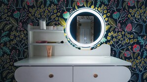 A vanity with a round mirror, a makeup brush, and a tube of lotion against a floral wallpaper. - The Leam Terrace Escape 3 Bed Townhouse (Royal Leamington Spa)
