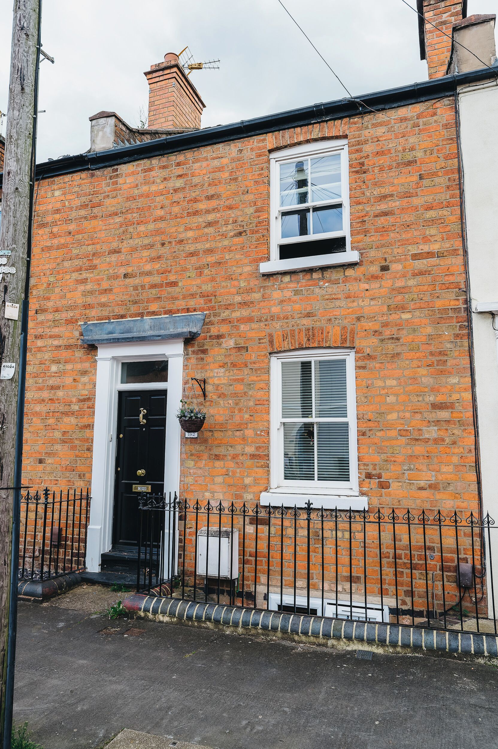 A two-story brick house with a black front door, a small window with shutters, and a white window above.