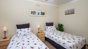 A hotel room with two beds, each with a bird-patterned duvet, a bedside table with a lamp, and a wall-mounted picture. - Headland Hideaway ~ Spectacular views for whale watching! (Kiama)