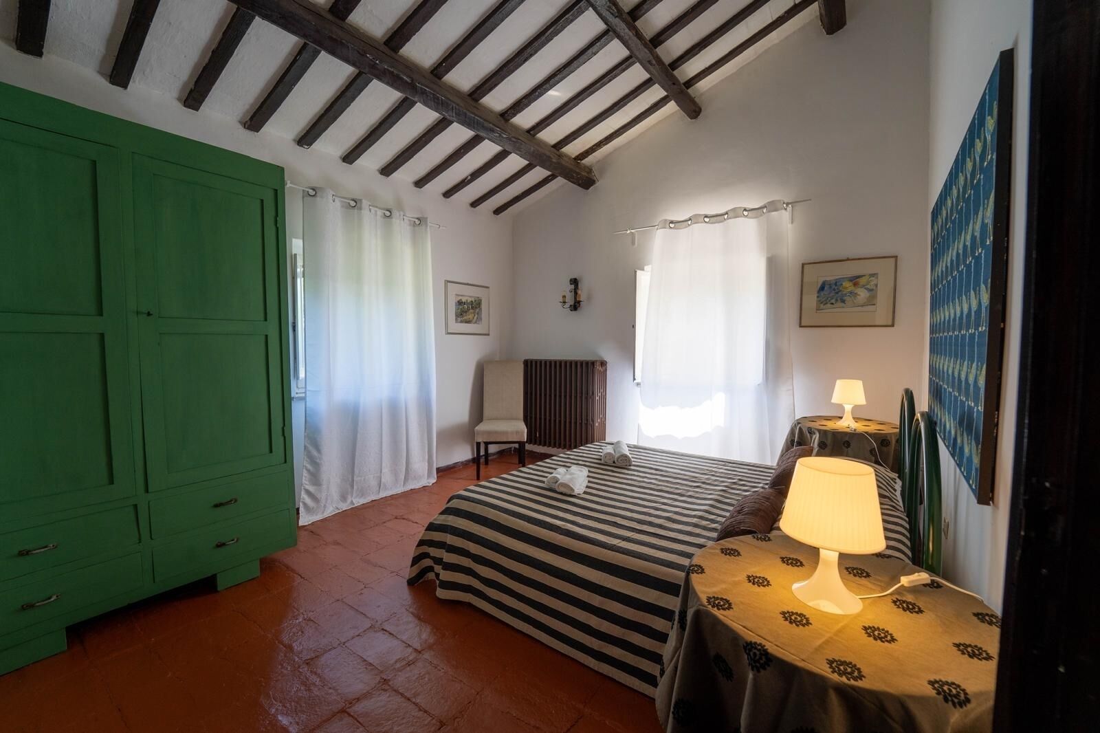 Une chambre à coucher avec un lit, une chaise, une table avec une lampe, un radiateur et une armoire verte.