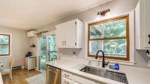 Una cocina moderna con armarios blancos, un lavamanos de acero inoxidable y una ventana con vistas a árboles.