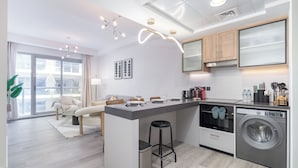 A modern kitchen with a built-in washer and dryer, a dining area with a sofa and table, and a large window providing natural light. - NEW Listing Just Renovated Beach Laguna (Ras Al Khaimah)