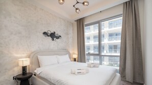 A hotel room with a large bed, a modern chandelier, a city view, and a small table with a lamp. - NEW Listing Just Renovated Beach Laguna (Ras Al Khaimah)