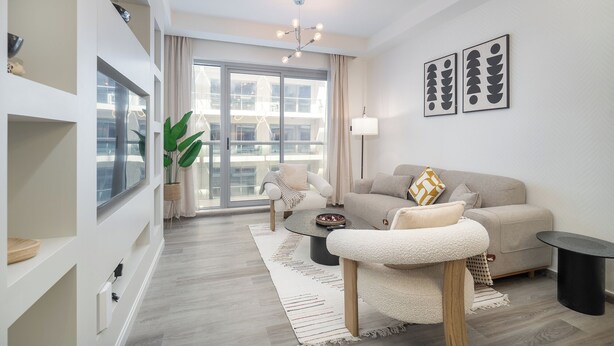 A modern living room with a grey sofa, a coffee table, and a large window with a view of a building. There are two framed artworks on the wall and a plant in the corner. - NEW Listing Just Renovated Beach Laguna (Ras Al Khaimah)