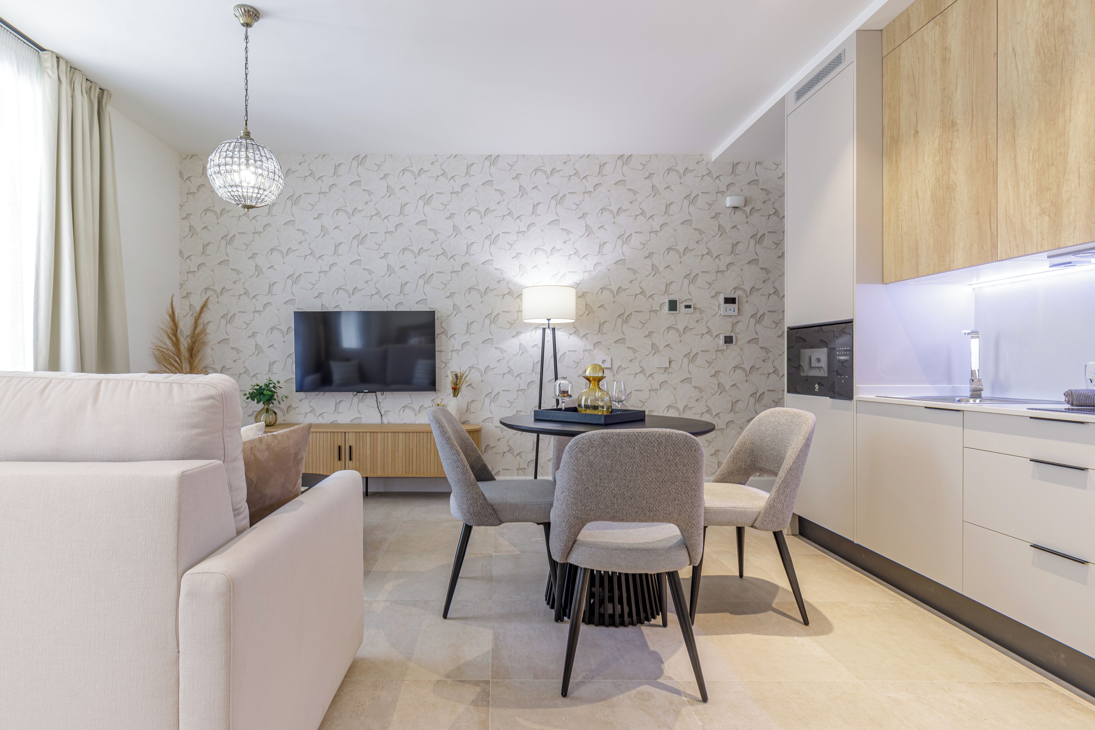 Een moderne woonkamer met een bank, een eettafel met stoelen, een televisie, en een keuken met kastjes en een aanrecht.