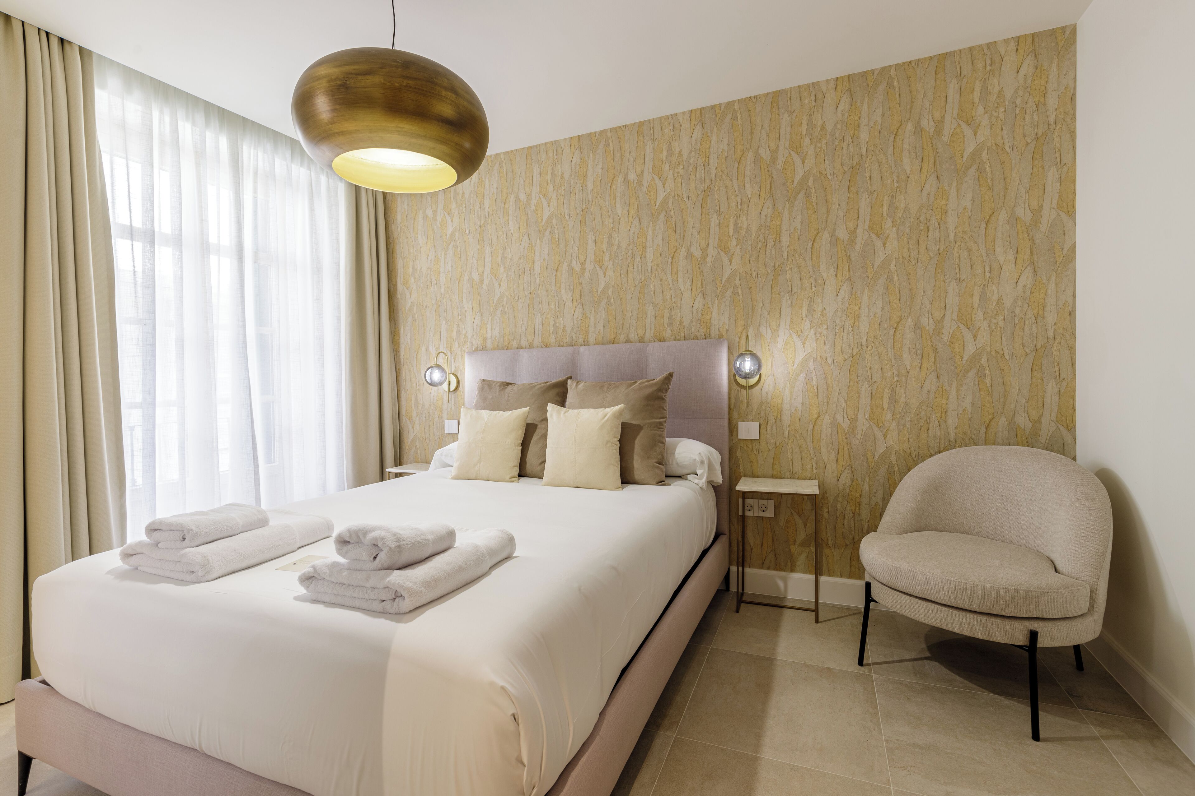 Una cama bien hecha con toallas dobladas, un cabecero moderno y una lámpara de pared.
